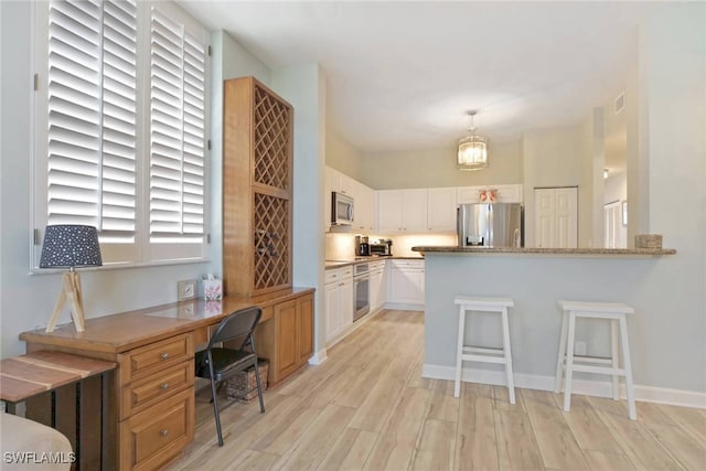 kitchen with hanging light fixtures, kitchen peninsula, white cabinetry, appliances with stainless steel finishes, and light wood-type flooring