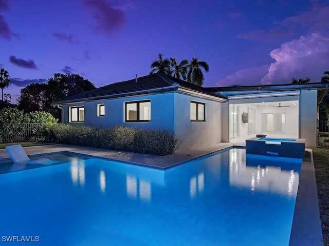 pool at dusk with a patio area and an in ground hot tub