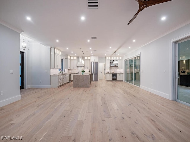 unfurnished living room featuring sink, ceiling fan with notable chandelier, ornamental molding, and light hardwood / wood-style floors