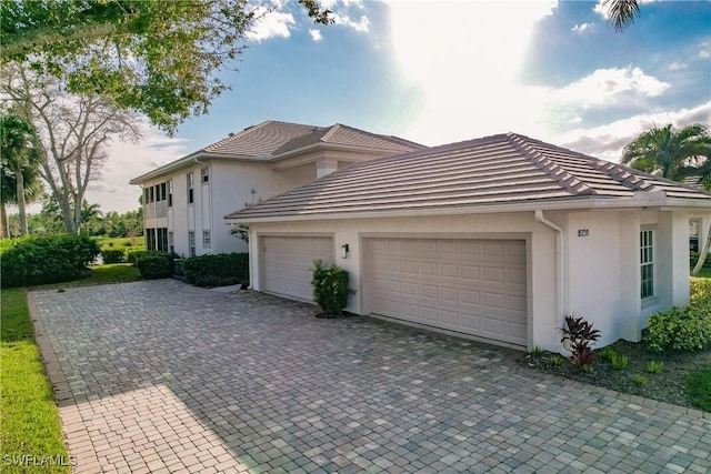 mediterranean / spanish-style house with an attached garage, a tile roof, decorative driveway, and stucco siding