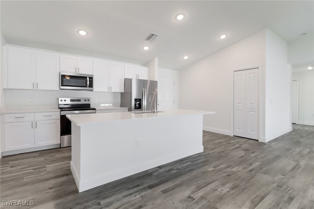 kitchen with appliances with stainless steel finishes, a kitchen island with sink, vaulted ceiling, and white cabinets