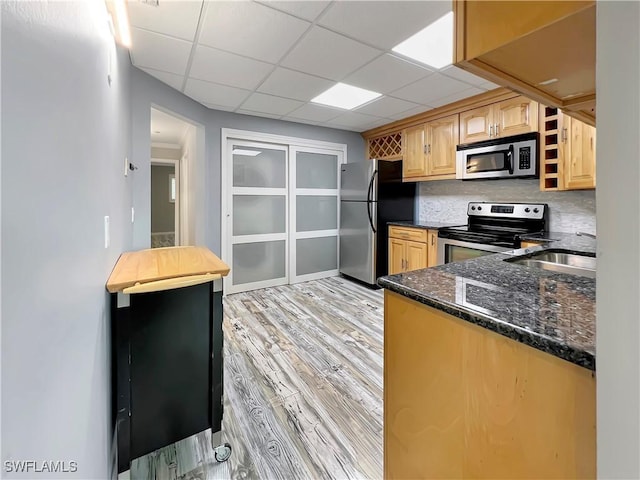 kitchen featuring stainless steel appliances, backsplash, dark stone counters, light hardwood / wood-style floors, and a paneled ceiling