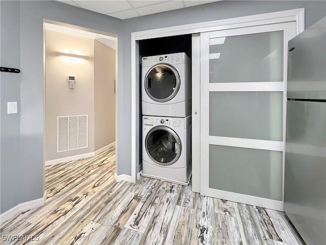 clothes washing area with stacked washing maching and dryer and light hardwood / wood-style flooring