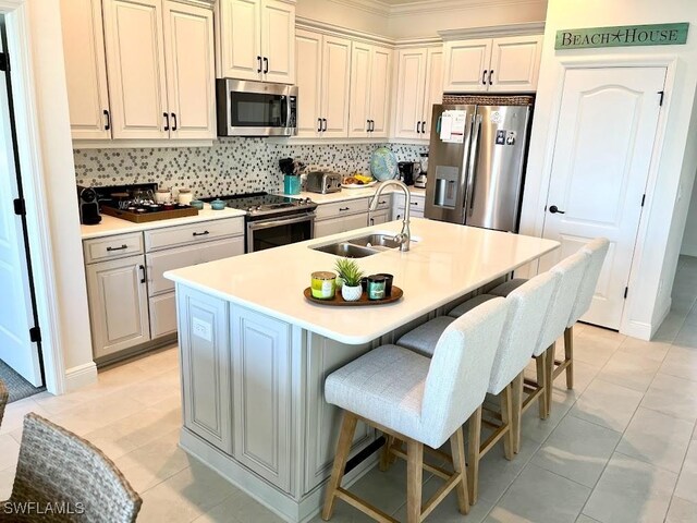 kitchen with appliances with stainless steel finishes, a kitchen bar, an island with sink, backsplash, and light tile patterned floors