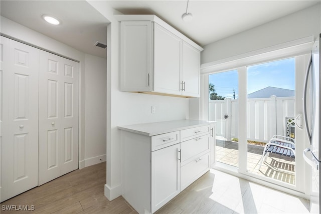 kitchen featuring light wood-type flooring, stainless steel fridge, and white cabinetry