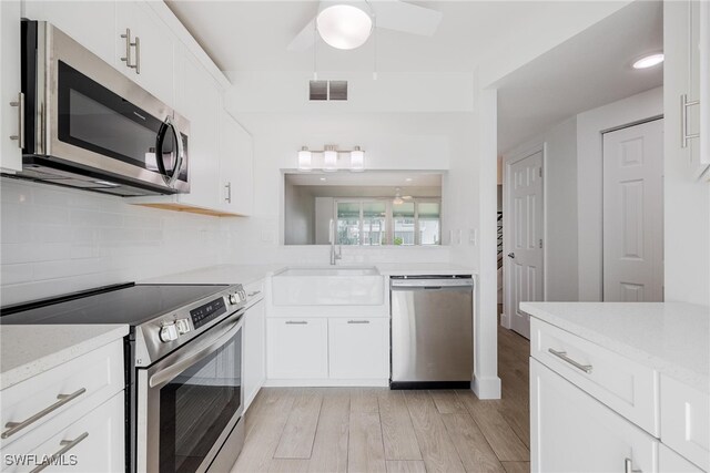 kitchen featuring white cabinets, sink, appliances with stainless steel finishes, light stone countertops, and light hardwood / wood-style floors