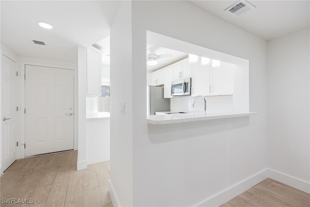 kitchen featuring stainless steel appliances, light hardwood / wood-style floors, kitchen peninsula, and white cabinetry