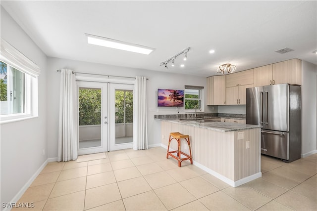 kitchen with dark stone countertops, a breakfast bar, kitchen peninsula, high quality fridge, and light brown cabinetry