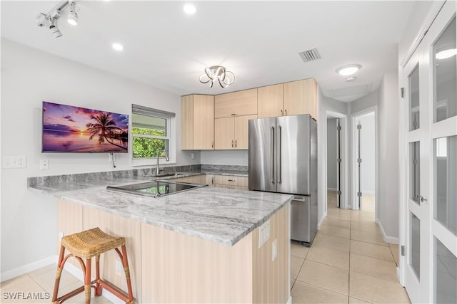 kitchen with light stone counters, stainless steel refrigerator, kitchen peninsula, light brown cabinets, and black electric stovetop