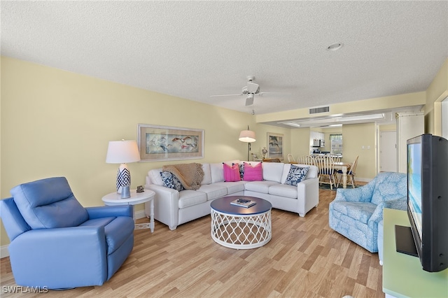 living room featuring a textured ceiling, light wood-type flooring, and ceiling fan