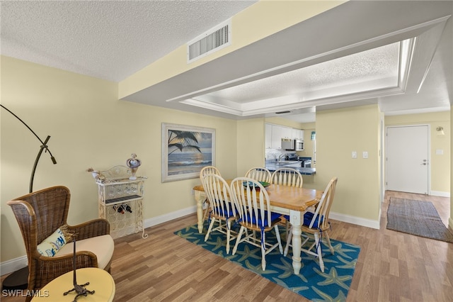 dining space with a textured ceiling, a raised ceiling, and light hardwood / wood-style flooring