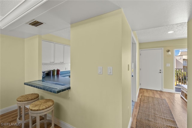 kitchen featuring tile countertops, a kitchen breakfast bar, a textured ceiling, light hardwood / wood-style flooring, and white cabinets