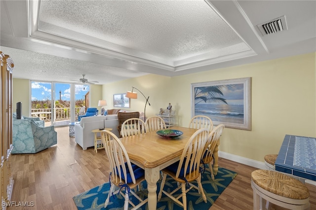 dining room featuring hardwood / wood-style flooring, ceiling fan, a textured ceiling, expansive windows, and a raised ceiling