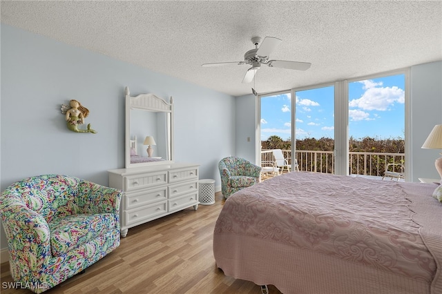 bedroom featuring a textured ceiling, access to exterior, a wall of windows, ceiling fan, and light hardwood / wood-style flooring