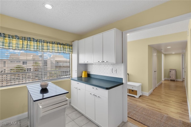 kitchen featuring white cabinets, decorative backsplash, light hardwood / wood-style floors, and a textured ceiling