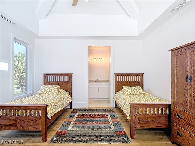 bedroom featuring wood-type flooring, ensuite bath, and beamed ceiling