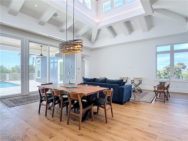 dining space featuring beamed ceiling, an inviting chandelier, light hardwood / wood-style flooring, and a towering ceiling