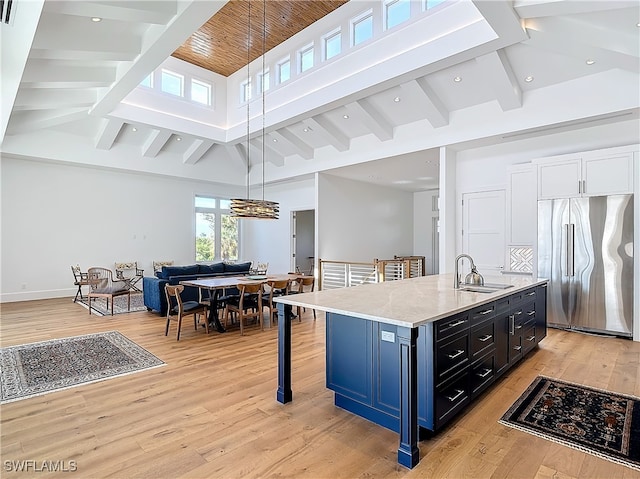 kitchen with an island with sink, pendant lighting, light hardwood / wood-style flooring, sink, and stainless steel built in fridge