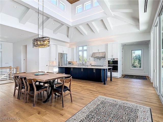 dining area with light wood-type flooring, sink, beamed ceiling, and high vaulted ceiling