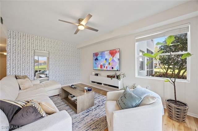 living area with ceiling fan, a wealth of natural light, an accent wall, and wallpapered walls