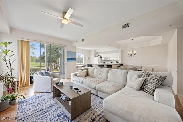 living room featuring light wood-style flooring, visible vents, baseboards, and ceiling fan with notable chandelier
