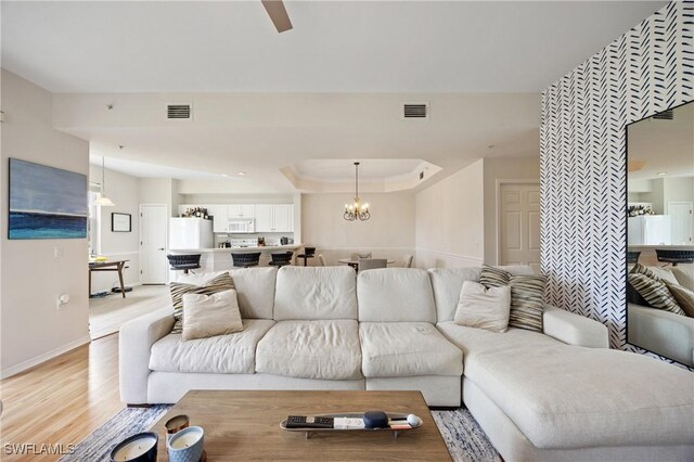 living area with baseboards, a tray ceiling, visible vents, and light wood-type flooring