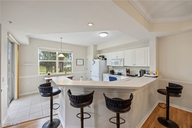 kitchen featuring a breakfast bar, white cabinets, decorative light fixtures, and white appliances