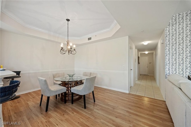 dining area featuring crown molding, light wood-style floors, a raised ceiling, a notable chandelier, and visible vents