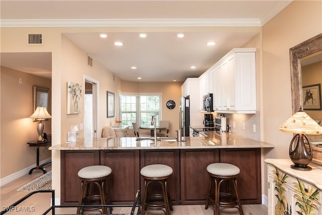 kitchen with stainless steel appliances, sink, light hardwood / wood-style floors, white cabinetry, and a breakfast bar area