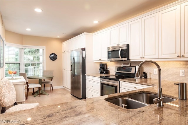 kitchen featuring sink, tasteful backsplash, light stone counters, white cabinets, and appliances with stainless steel finishes