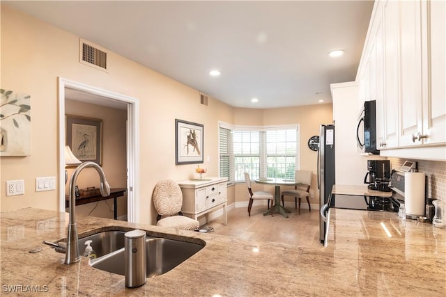 kitchen featuring backsplash, range, sink, light stone countertops, and white cabinetry