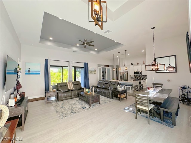 living room featuring ceiling fan with notable chandelier, light wood-type flooring, and a raised ceiling