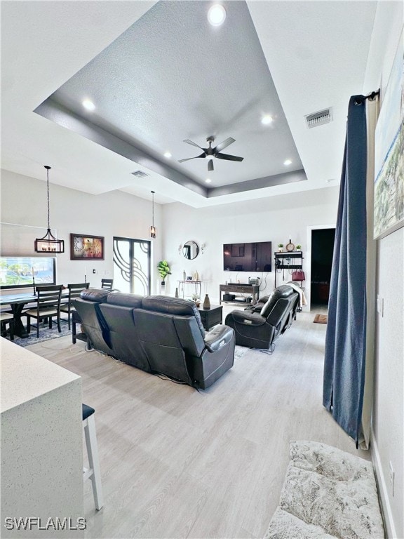 living room featuring a raised ceiling, a textured ceiling, light wood-type flooring, and ceiling fan with notable chandelier