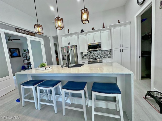 kitchen with a large island with sink, light hardwood / wood-style flooring, pendant lighting, white cabinetry, and appliances with stainless steel finishes