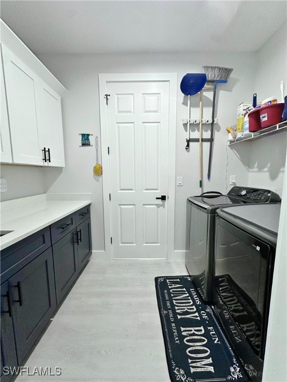 clothes washing area featuring washing machine and clothes dryer, light wood-type flooring, and cabinets