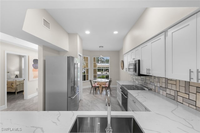 kitchen with light stone countertops, stainless steel appliances, white cabinets, and pendant lighting