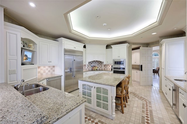 kitchen featuring a raised ceiling, a sink, and built in appliances