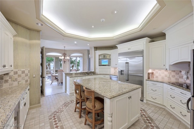 kitchen with a kitchen island, a peninsula, a tray ceiling, stainless steel appliances, and backsplash