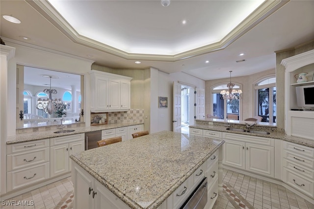 kitchen with a tray ceiling, a sink, a notable chandelier, and dishwashing machine