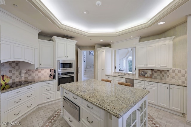 kitchen with stainless steel appliances, a sink, white cabinets, a warming drawer, and a tray ceiling