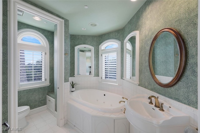 bathroom featuring wallpapered walls, toilet, a sink, baseboards, and a tub with jets