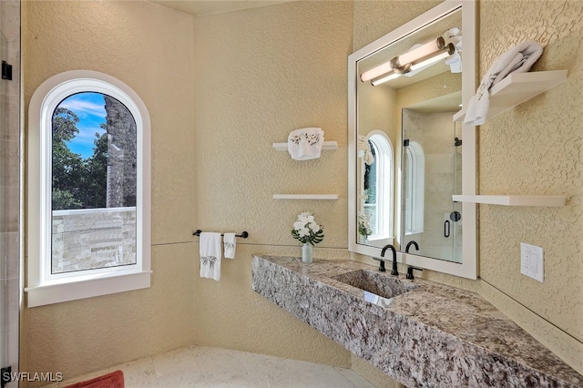 full bath featuring a shower with shower door, a sink, and a textured wall