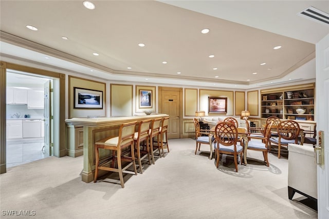 carpeted dining space featuring a raised ceiling, ornamental molding, and indoor bar