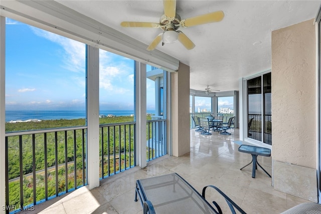 sunroom with ceiling fan and a water view