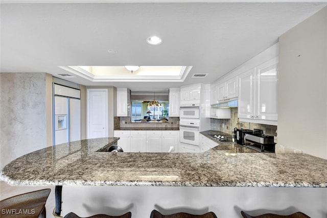 kitchen with white cabinets, a kitchen breakfast bar, kitchen peninsula, and white appliances