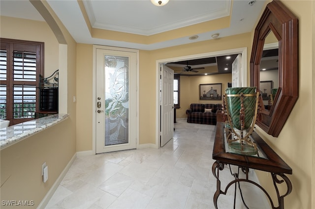 foyer with ornamental molding, ceiling fan, and a raised ceiling