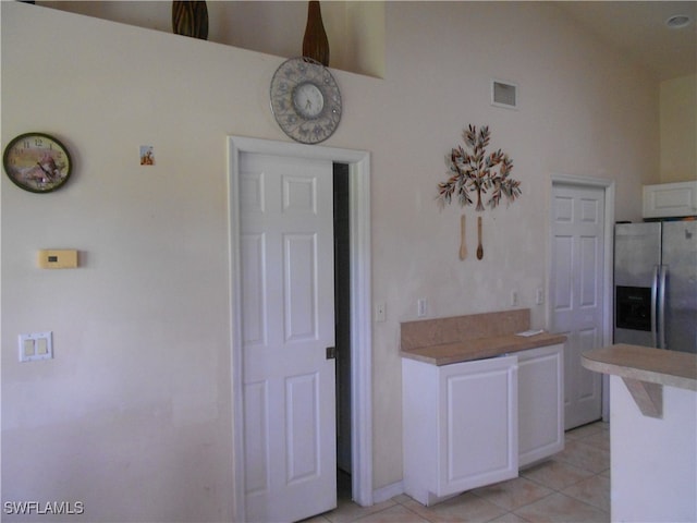 kitchen with white cabinetry, light tile patterned flooring, a high ceiling, and stainless steel refrigerator with ice dispenser