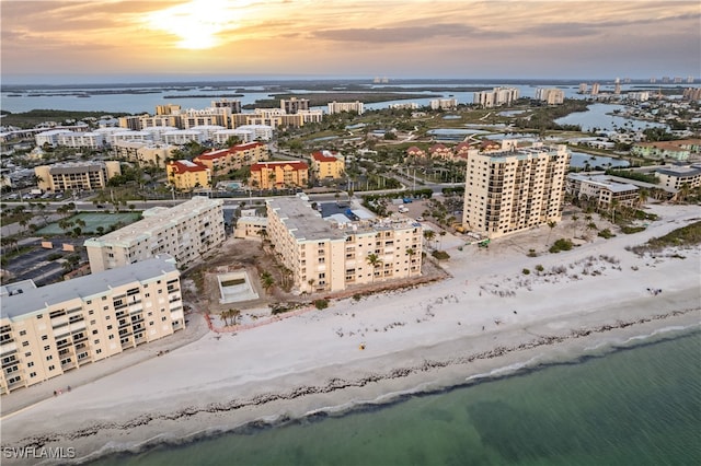 aerial view at dusk featuring a view of the beach and a water view