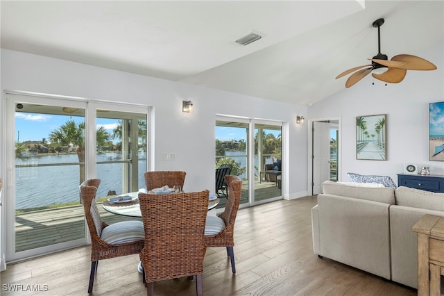 dining area featuring ceiling fan, a water view, vaulted ceiling, and light hardwood / wood-style floors