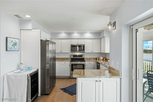 kitchen featuring stainless steel appliances, white cabinetry, kitchen peninsula, light stone countertops, and light wood-type flooring